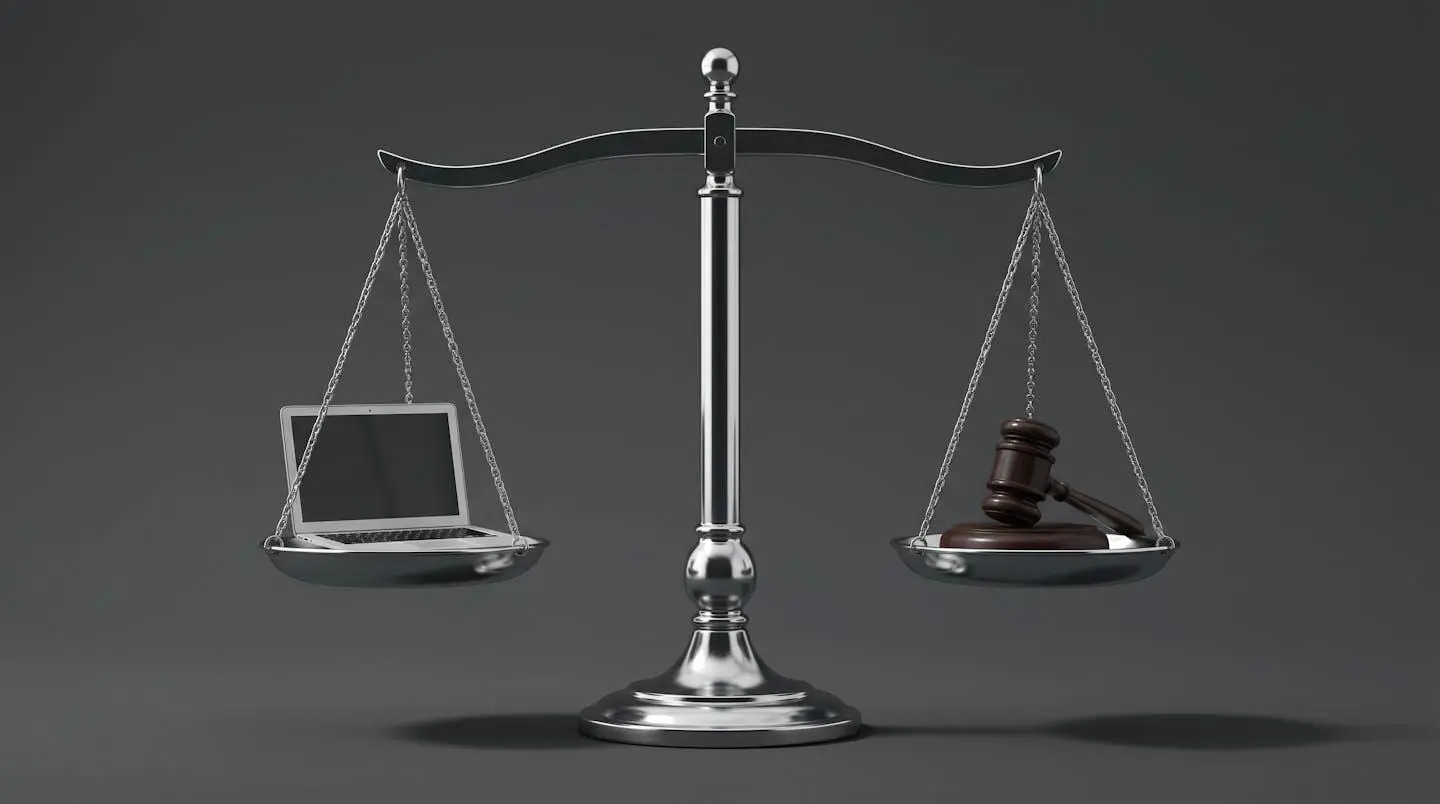 Photographie d'une balance de justice en équilibre, avec un ordinateur miniature sur un plateau et un marteau de juge sur l'autre, symbolisant la tension entre technologie et légalité